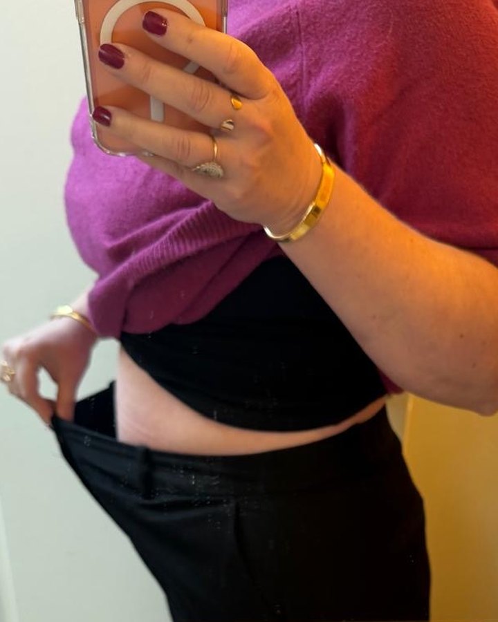 A client holds up her old trousers, now too big for her, face hidden