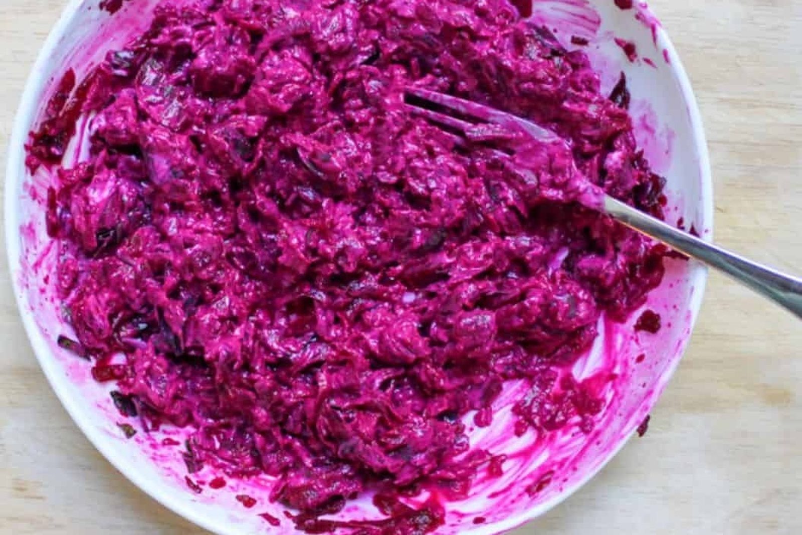 Bright pink grated beetroot mixed with yoghurt in a white bowl, with a fork