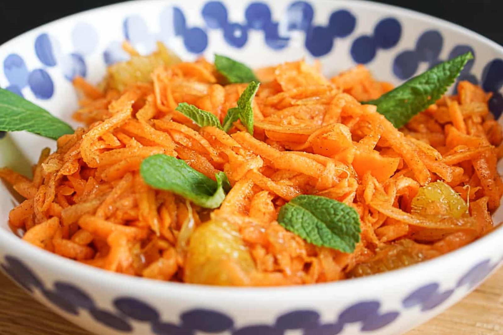 Carottes râpées avec des morceaux d'orange, des raisins secs et quelques feuilles de menthe, dans un bol à pois bleus