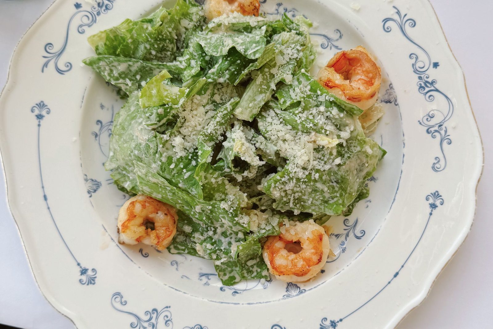 Caesar salad with romaine, parmesan and grilled prawns on a blue-patterned plate