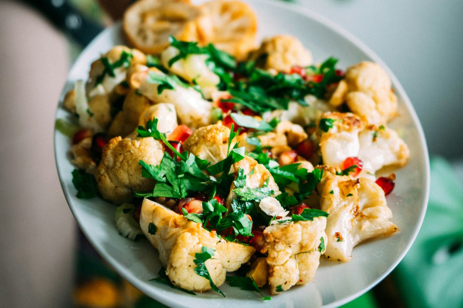 Roast cauliflower with herbs on a white plate held in one hand