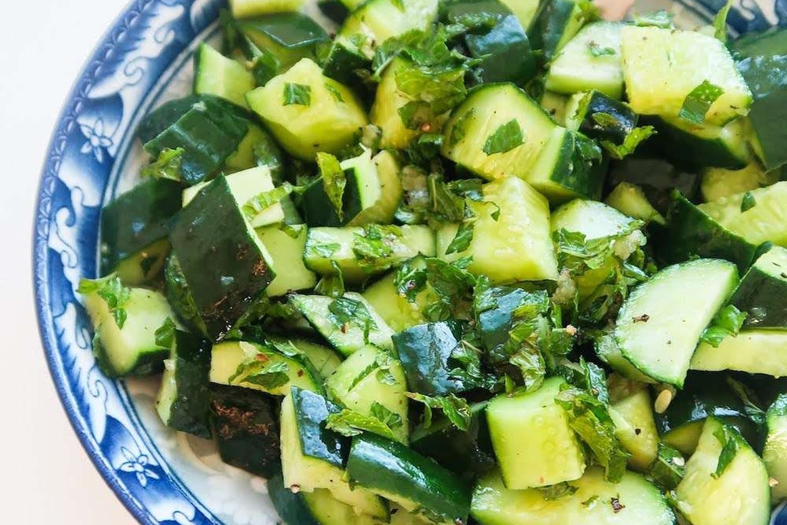 Diced cucumber and chopped mint in a blue-patterned bowl