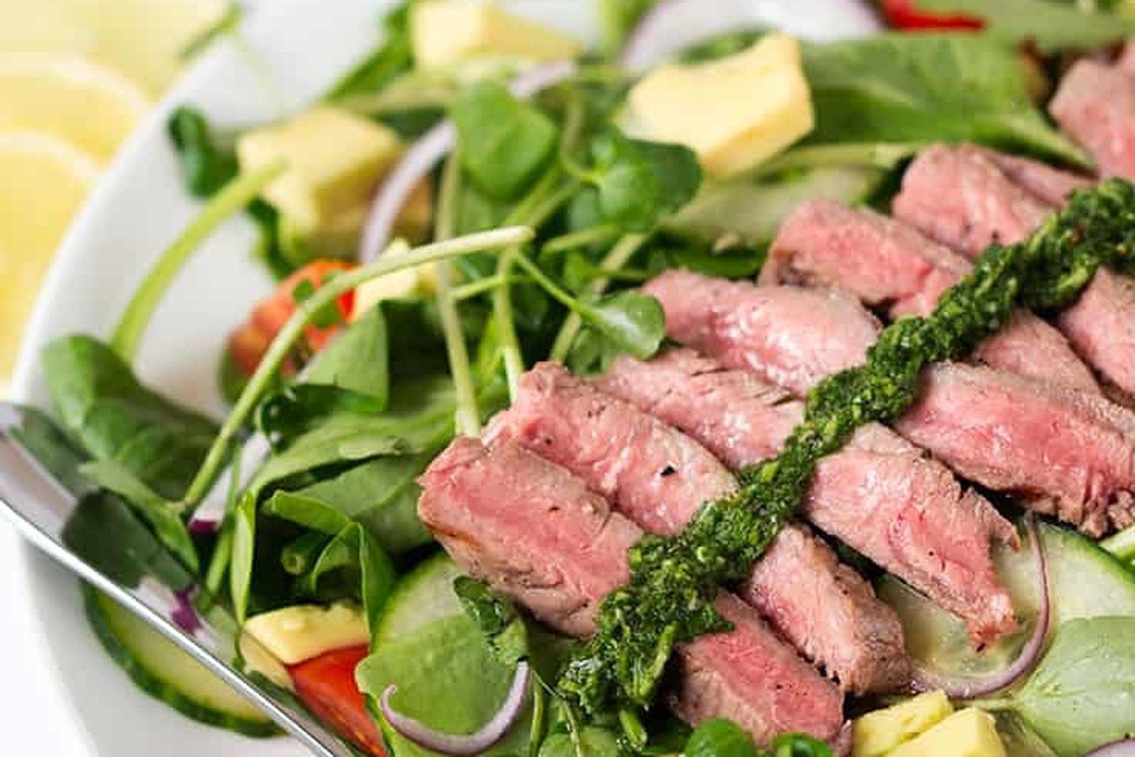 Fatias de bife malpassado com chimichurri sobre espinafre, abacate, pepino e tomate-cereja, com um garfo