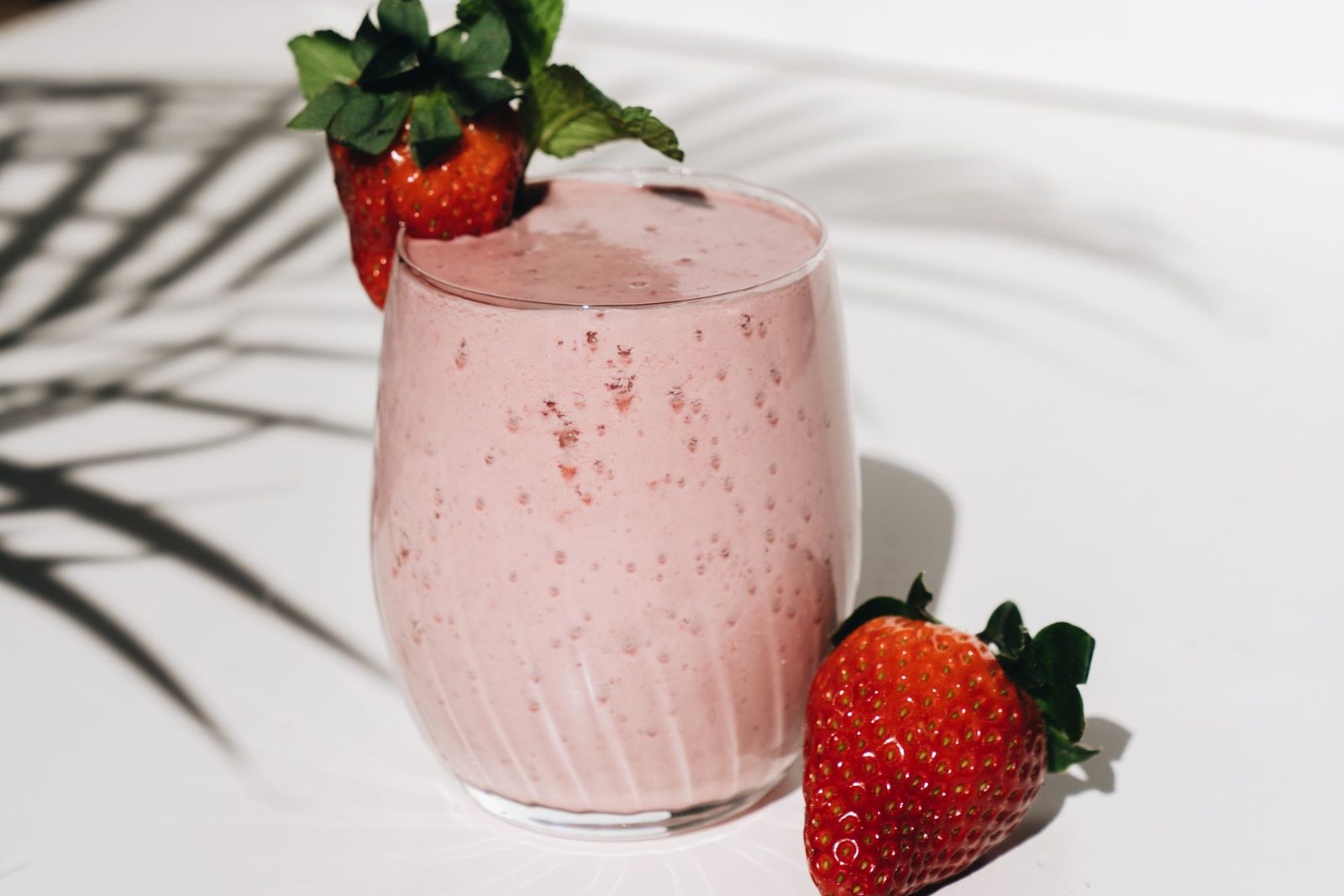 Smoothie rosa de morango num copo, com morangos ao lado