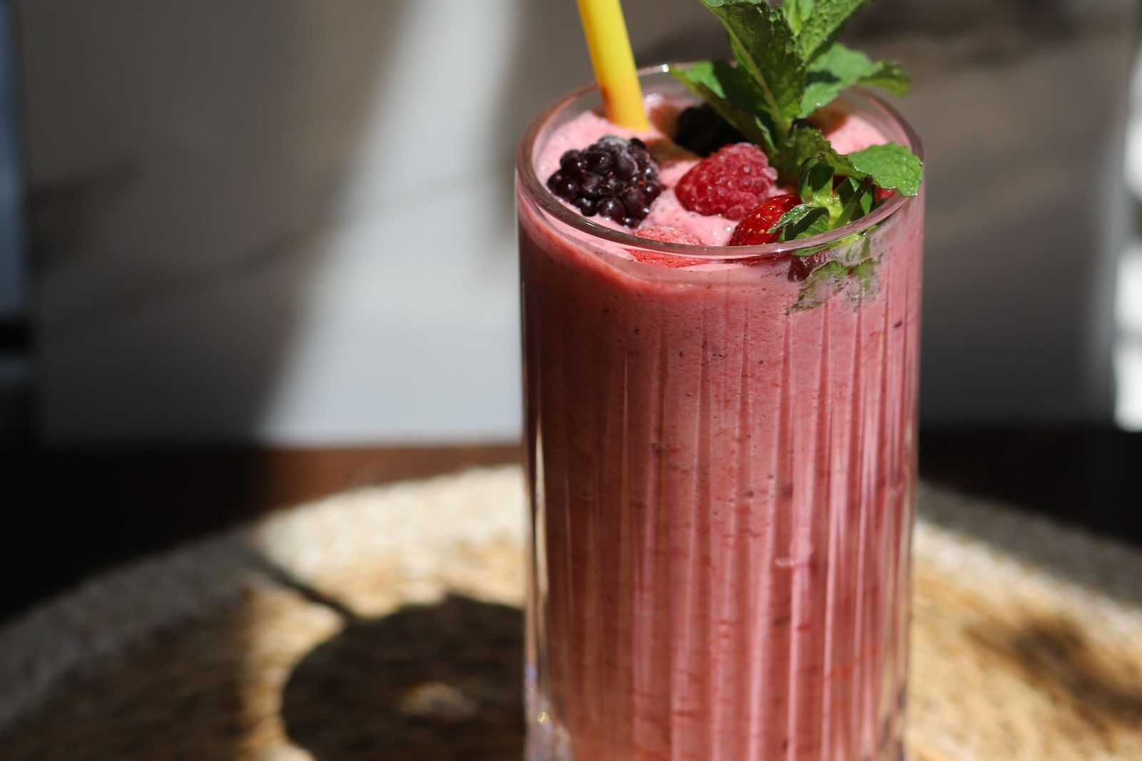 Red smoothie in a tall glass with mint, blackberries and a yellow straw