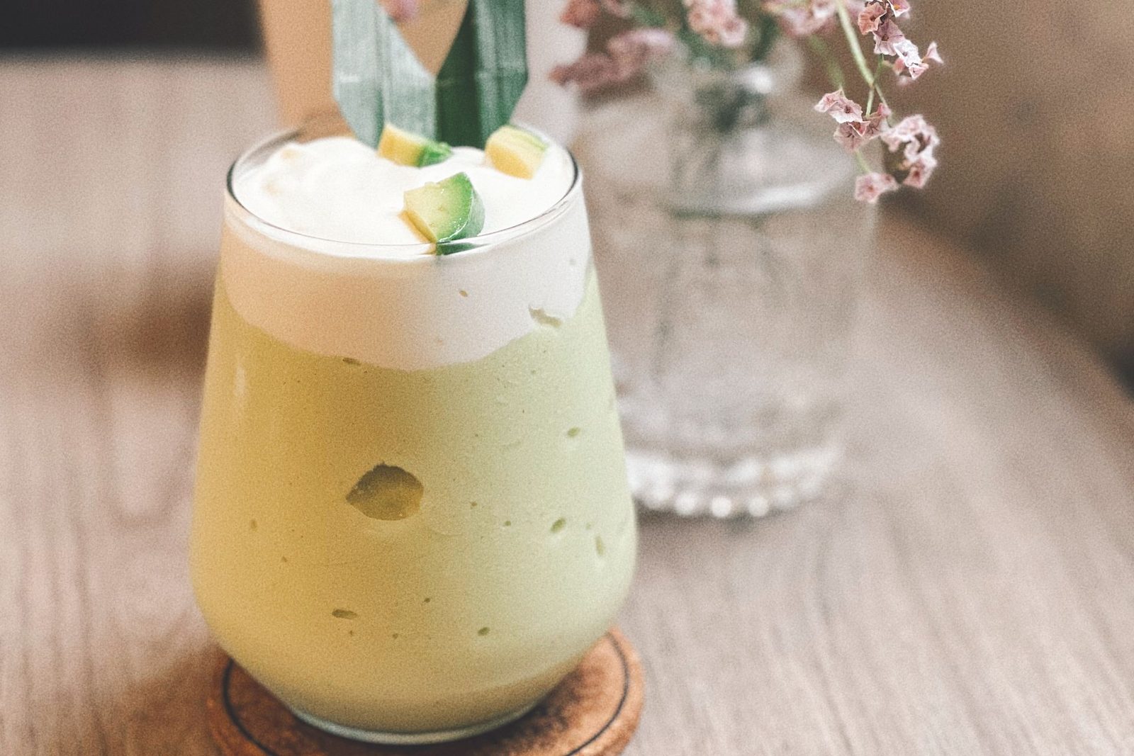 Green smoothie in a glass next to a vase of flowers